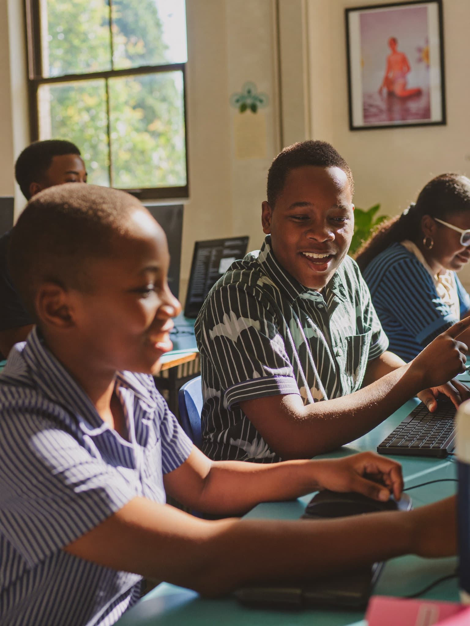Two Ghanaian students smiling as they learn together at a classroom computer in warm daylight